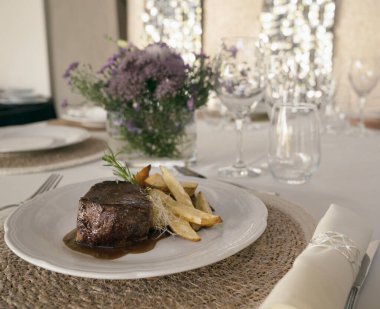 Gurme gastronomi. Düğün ana yemeği. Yakından bakınca kırmızı şarap soslu ızgara fileto ve masada güzel bir cam eşyalar ve sofra takımı ile patates.
