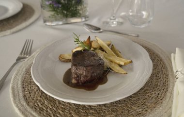 Gurme gastronomi. Düğün ana yemeği. Yakından bakınca, kırmızı şarap soslu ızgara fileto ve masada güzel kurulmuş patatesler görünüyor.