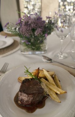 Gurme gastronomi. Düğün ana yemeği. Yakından bakınca kırmızı şarap soslu ızgara fileto ve masada güzel bir cam eşyalar ve sofra takımı ile patates.