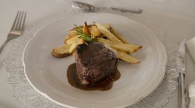 Gurme gastronomi. Düğün ana yemeği. Yakından bakınca, kırmızı şarap soslu ızgara fileto ve masada güzel kurulmuş patatesler görünüyor.