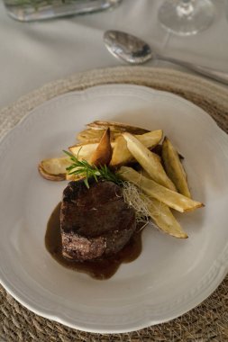 Gurme gastronomi. Düğün ana yemeği. Kırmızı şarap soslu ızgara fileto ve masada beyaz bir tabakta patates.