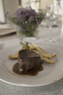Gurme gastronomi. Düğün ana yemeği. Yakından bakınca kırmızı şarap soslu ızgara fileto ve masada güzel bir cam eşyalar ve sofra takımı ile patates.