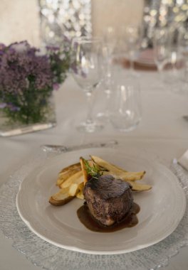 Gurme gastronomi. Düğün ana yemeği. Yakından bakınca kırmızı şarap soslu ızgara fileto ve masada güzel bir cam eşyalar ve sofra takımı ile patates.