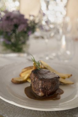 Gurme gastronomi. Düğün ana yemeği. Yakından bakınca kırmızı şarap soslu ızgara fileto ve masada güzel bir cam eşyalar ve sofra takımı ile patates.