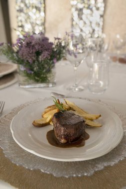 Gurme gastronomi. Düğün ana yemeği. Yakından bakınca kırmızı şarap soslu ızgara fileto ve masada güzel bir cam eşyalar ve sofra takımı ile patates.