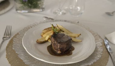 Gurme gastronomi. Düğün ana yemeği. Yakından bakınca kırmızı şarap soslu ızgara fileto ve masada güzel bir cam eşyalar ve sofra takımı ile patates.