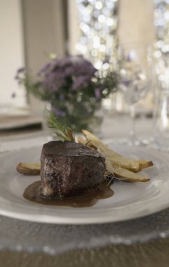 Gurme gastronomi. Düğün ana yemeği. Yakından bakınca kırmızı şarap soslu ızgara fileto ve masada güzel bir cam eşyalar ve sofra takımı ile patates.