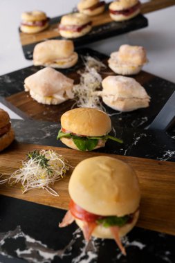 Sosyal bir etkinlikte gurme parmak yiyeceği. Yemek ve soğuk masa. Tavuk ve prosciutto mini sandviçlerinin yakın görüntüsü siyah mermer tabaklarda sunuluyor.