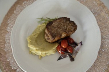 Gurme ana yemek. Kızarmış domuz filetosu, yanında patates püresi ve vişneli domates, beyaz bir tabakta.