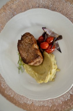 Gurme ana yemek. Kızarmış domuz filetosu, yanında patates püresi ve vişneli domates, beyaz bir tabakta.