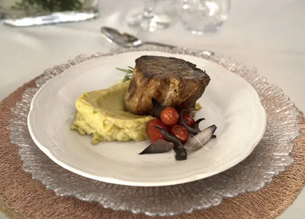 Gurme ana yemek. Kavrulmuş domuz filetosu, yanında patates püresi ve vişneli domates, beyaz bir tabakta.