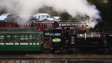 Tierra del Fuego, Arjantin 04,25,2025: Yağmurlu bir sabahta istasyonda park edilmiş popüler Austral Fueguino buharlı lokomotifi ve yeşil vagonların görüntüsü. Siyah lokomotiften beyaz buhar çıkıyor. Baş mühendis içeride..