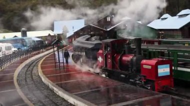 Tierra del Fuego, Arjantin 04,25,2025: Dünya demiryolunun tarihi sonu. Kırmızı lokomotiften beyaz buhar çıkıyor. Ormandaki tren ve istasyon manzarası