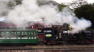 Tierra del Fuego, Arjantin 04,25,2025: İstasyona park edilmiş Austral Fueguino buharlı lokomotifi ve yeşil vagonlar. Baş mühendis içeride.