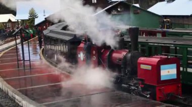 Tierra del Fuego, Arjantin 04,25,2025: Demiryolu Austral Fueguino kırmızı buhar lokomotifi ve vagonları, yağmurlu bir sabahta istasyona park edildi. Lokomotifin içindeki baş mühendis.