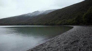Göle düşen yağmur damlaları. Tierra del Fuego Ulusal Parkı 'nda yağmurlu ve bulutlu bir sabahta yeşil orman ve tepelerle çevrili turkuaz buzul gölü manzarası
