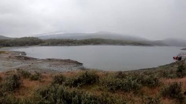Patagonya manzarası. Tierra del Fuego Ulusal Parkı 'nda yağmur yağıyor. Göl manzarası ve bulutlu bir gökyüzünün altındaki dağlar. Çimenlere ve su yüzeyine düşen yağmur damlaları
