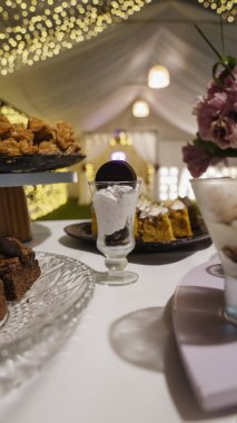 Doğum günü için yemek servisi. Kurabiye ve kremalı tatlıyla dolu tatlı masasının yakın görüntüsü. Işıklar, çiçek aranjmanı ve arka plandaki çadır.