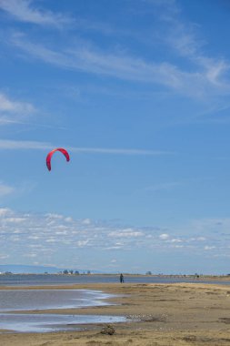 Deserted sandy beach with a kitesurfer in the distance. clipart