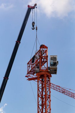 Sayaç yelkeni takıldı. Kırmızı mobil vinç mavi gökyüzünün arka planında sarı kule vincinin bir bölümünü kaldırıyor.