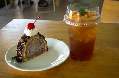 Beyaz tabakta kirazlı çikolatalı pasta ve şeftalili buzlu çay.