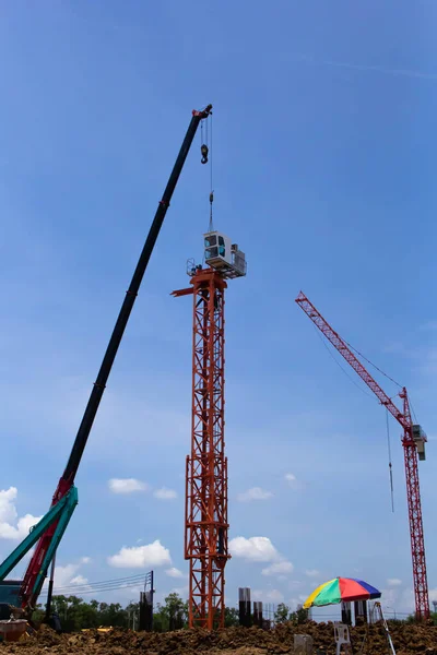 The Counter Jib Is Installed. Red mobile crane lifts a section of yellow tower crane on a background of blue sky