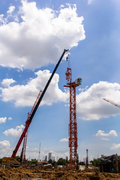 The Counter Jib Is Installed. Red mobile crane lifts a section of yellow tower crane on a background of blue sky