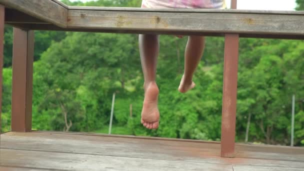 女の子はテラスに座って スイング脚 リラックス リラックス 一人で 美しい自然の山の森を持つ木の家で静かでプライベート — ストック動画