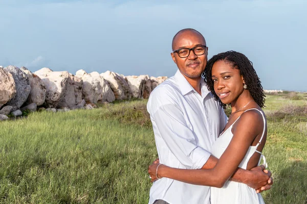 Stock image Young black couple share close embrace outside in a grass field on a sunny day. Jamaican couple