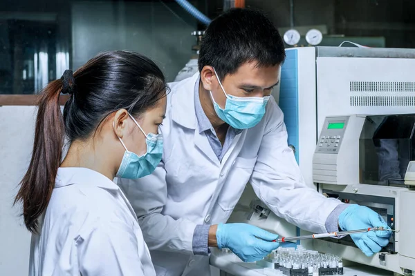 The male researcher prepares a column chromatography cartridge of the Liquid Chromatography mass spectrometry LC-MS instrument to analyze and train a female scientist to use the instrument.