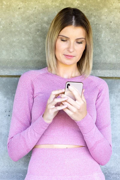 Happy fit woman wearing active wear or sports apparel counts calories and made post in blog after fitness workout. Healthy girl wearing sportwear hold smartphone in hand and considers calories in