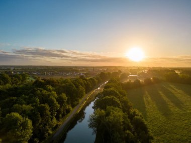 Güneşin doğuşunu ya da batışını gösteren bir dron tarafından çekilen hava görüntüsü ve ağaçları sıcak akşam ışığı ile dolduran sis, altın ışık ışınlarıyla yükseliyor. Bulutlar ve bulutlar yansıyor
