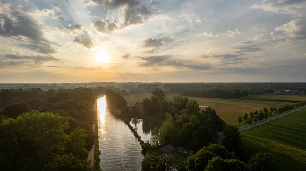 Stock image Aerial view, shot by a drone, of the sun rising or setting behind the river and fills the trees with warm evening light, fog rises in the rays of golden light. Clouds and clouds are reflected in the