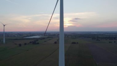 Drone, güneş doğarken kırsal bir arazide sis eşliğinde rüzgar türbini çiftliği vurdu. Yakın çekim rüzgar türbinleri gün doğumunda. Yel değirmenleri yeşil enerji üretiyor. Büyük rüzgâr türbinleri, parlak turuncu pervaneli.