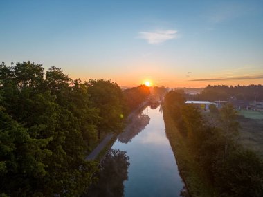 Güneşin doğuşunu ya da batışını gösteren bir dron tarafından çekilen hava görüntüsü ve ağaçları sıcak akşam ışığı ile dolduran sis, altın ışık ışınlarıyla yükseliyor. Bulutlar ve bulutlar yansıyor