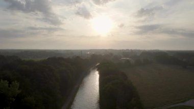 Yeşil çalıları ve çarpıcı zengin gökyüzü olan bir nehrin üzerinde güzel puslu bir gün batımı. Yüksek kalite 4k görüntü