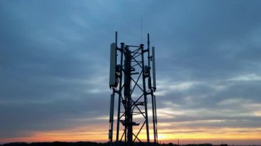 Rise up reveal footage shot by a drone of 3G, 4G, 5G. Mobile phone base station Tower. Development of communication system in non-urban forest area with dark sunset or sunrise sky background. High
