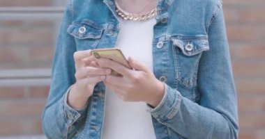 Şık giyinmiş ve kot ceketli beyaz bir kadın bir şey bulmak için akıllı telefon kullanıyor. Yüzü yok. Ön manzara. Yüksek kalite 4k görüntü