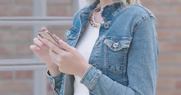 ファッショナブルな服装の若い白人女性と青いジーンズのジャケットは何かを見つけるためにスマートフォンを使用しています 顔はない サイドビュー 高品質4K映像 — ストック動画