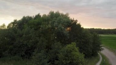 İnsansız hava aracı Belçika 'da sonbaharda bulutlu bir günbatımında göl ve ağaçların üzerinden uçarak yükseliyor ve gökyüzü de suya yansıyor. Yüksek kalite 4k görüntü