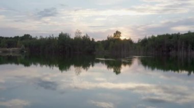 Orman ağaçları gölün sessiz yüzeyine yansıyor, çok huzurlu, insan yok, gölde dramatik gökyüzü yansıması. Yüksek kalite 4k görüntü