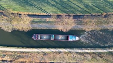 Güneşli bir kış gününde bir kargo kanalı gemisinin hava görüntüsü kanaldan geçer, suda yansımalar görülür, Belçika, Rijkevorsel 'in eteklerindeki kanal sistemi. Yüksek