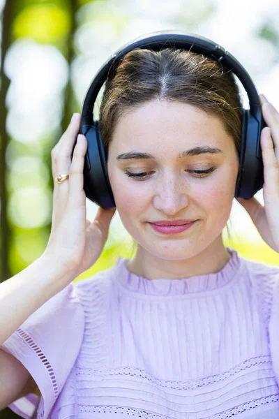 Kulaklıklı kadın, yakından müzik dinliyor, özgür ve dışarıda teknolojiyle mutlu. Model mekan, podcast veya radyo yayını, yeşil ayar ve ses listesindeki kadın. Yüksek