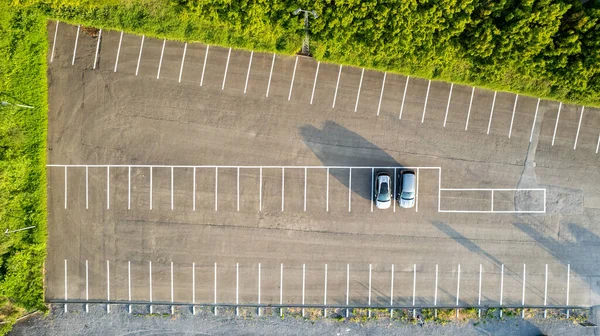 Güneş doğarken parketmiş iki arabalı neredeyse boş bir otoparkın havadan görüntüsü uzun gölgeler bırakıyor. Yüksek kalite fotoğraf