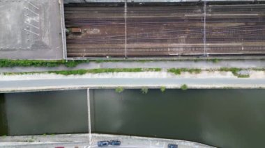 Açık bir günde Belçika 'nın Halle şehrindeki bir nehrin yanındaki tren raylarının yukarıdan çekilmiş insansız hava aracı görüntüsü. Köprünün altından bir tren geçiyor. Yüksek kalite 4k görüntü