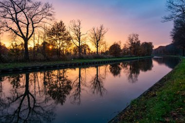 Doğanın büyüleyici güzelliğine tanık olun dramatik ve renkli bir günbatımı gökyüzü nehrin sakin sularına yansıyan ağaç siluetleriyle nefes kesici bir tuval çiziyor. Gökyüzü