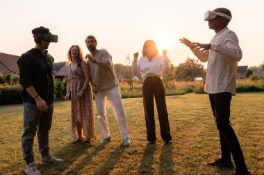 Genç, çok ırklı arkadaş grubunun bahçede günbatımına karşı fütüristik sanal gerçeklik gözlükleriyle simülasyon deneyimi var. İki arkadaş birbirine karşı oynuyor.