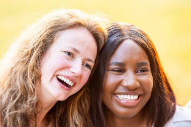 İki kadın arkadaş arasındaki güçlü bağı yansıtan yürek ısıtan bir portre. Biri beyaz, diğeri siyah. Kafaları birbirine yakın, ve bakışlarını kaçırarak samimi bir gülümseme sergiliyorlar.