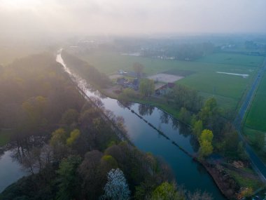 Mistik bir sabahın büyüleyici güzelliğine dalın. Kamera büyüleyici bir nehir, çiftlik arazisi ve orman manzarasının havadan görüntüsünü yansıtıyor. Sabahın usulca kucaklamasında
