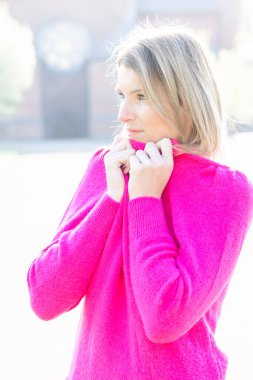 Yürek ısıtan bir manzara, genç bir milenyum kadınının kendi kozasında teselli bulması gibi. Yumuşak pembe bir kazağa sarılmış, yüzünü nazikçe gizliyor, sıcaklığın ve yumuşaklığın tadını çıkarıyor.